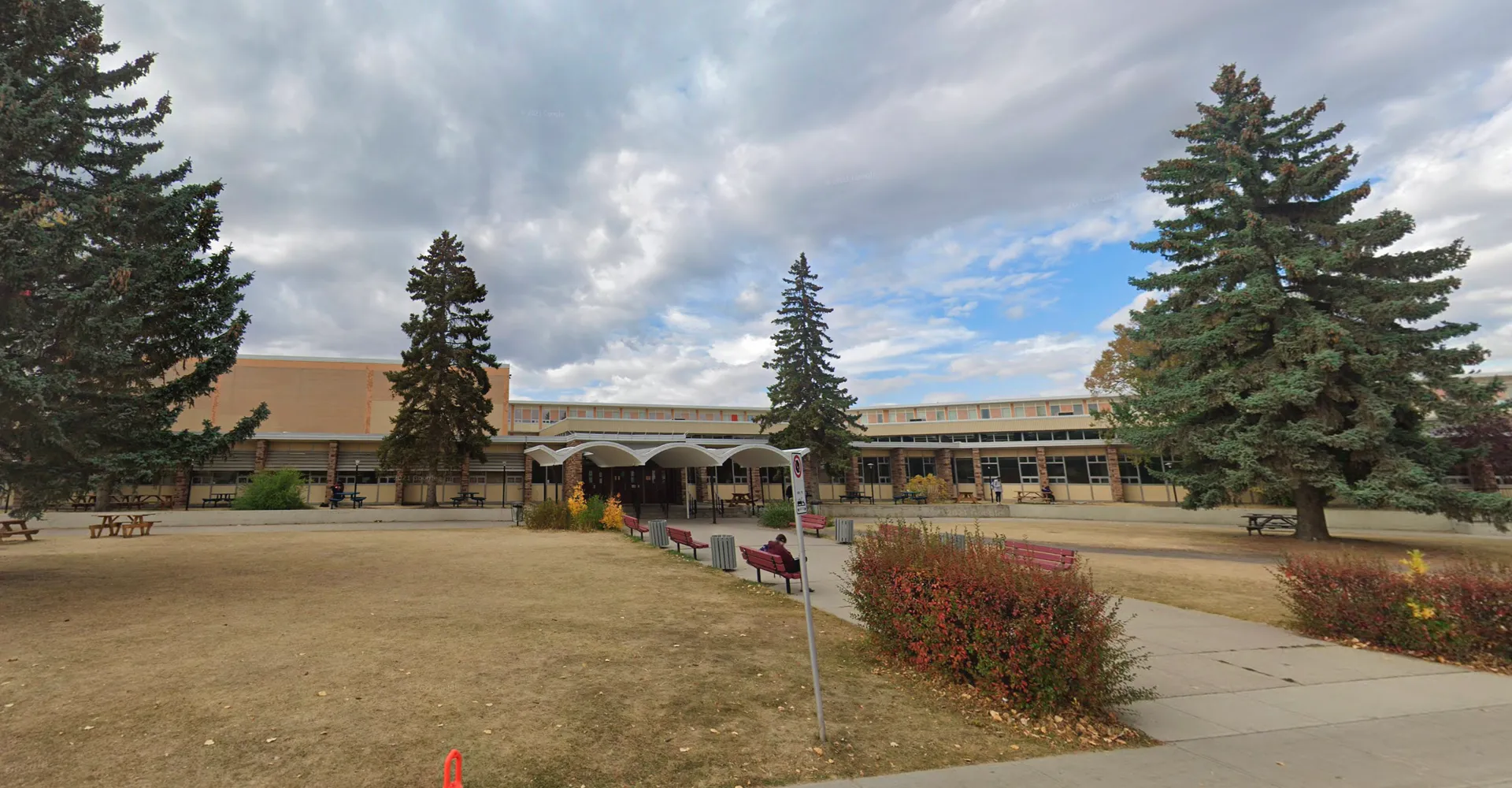L'edificio principale a più piani della Henry Wise Wood High School con ingresso coperto e uno spazio verde in primo piano sotto un cielo nuvoloso.