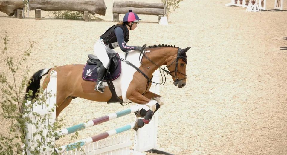 Una studentessa della Charterhouse School salta un ostacolo con il suo cavallo in un campo all'aperto.
