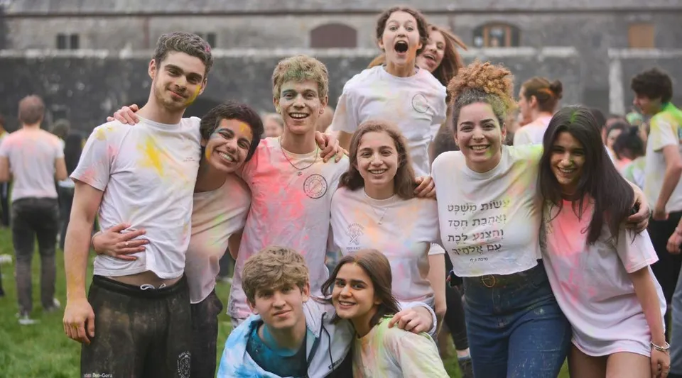 Un gruppo di studenti e studentesse si trova insieme su un prato davanti a un edificio del campus del UWC Atlantic College.