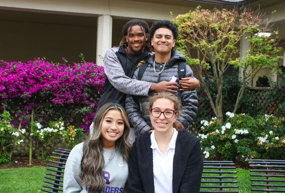 Un gruppo di quattro studenti posa insieme in un giardino con fiori colorati nel campus della Archbishop Riordan High School.