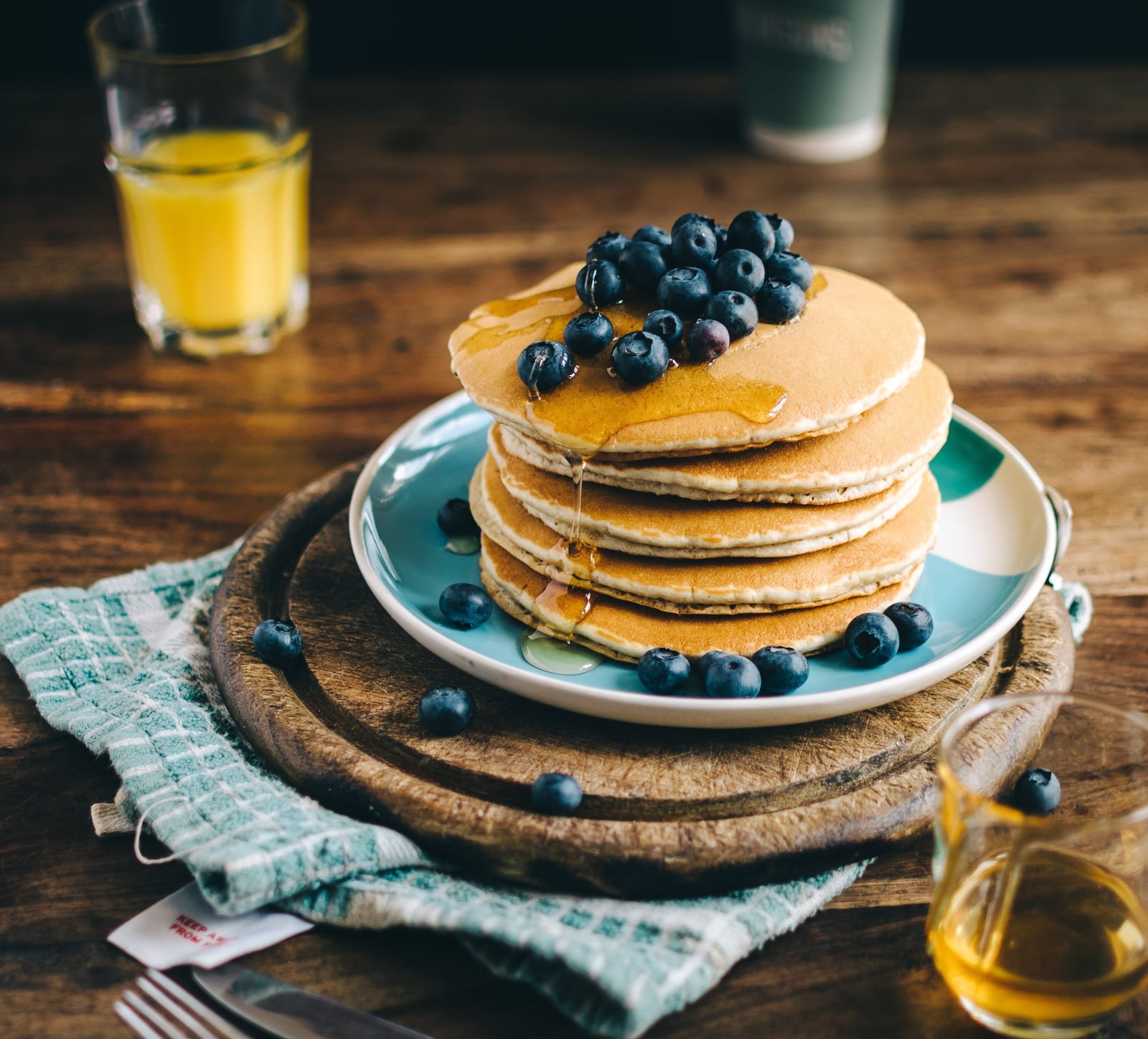Stapel Pfannkuchen mit Blaubeeren und Sirup, daneben ein Glas Orangensaft