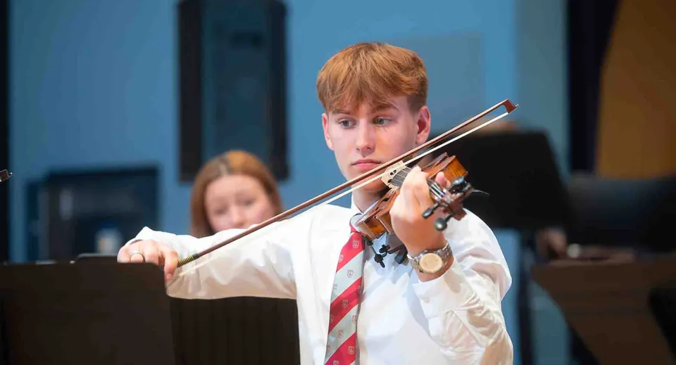 Un studente della Warwick School con camicia bianca e cravatta suona il violino.