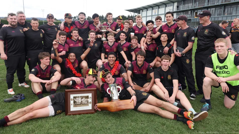 Un gruppo di studenti della Hamilton Boy's High School posa sul campo sportivo tenendo una coppa dopo una vittoria.