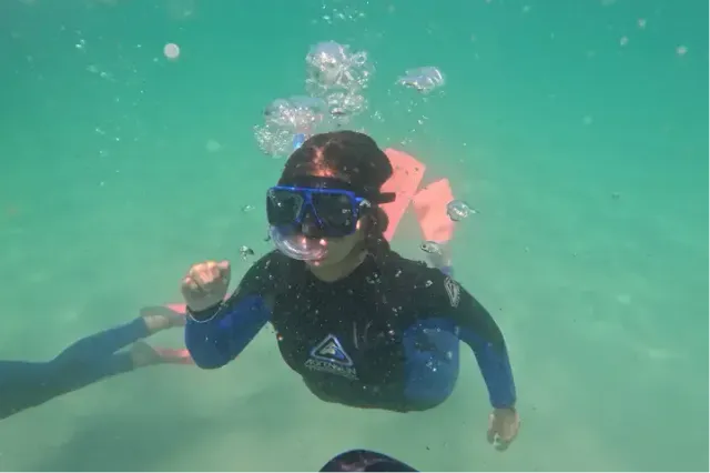 Ragazza fa snorkeling sott'acqua indossando una muta