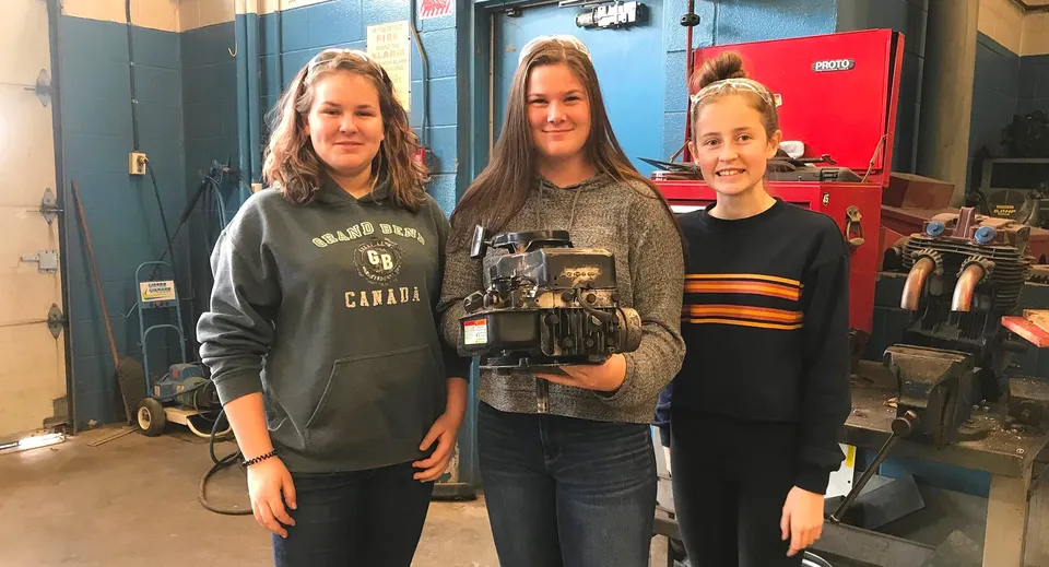 Tre studentesse sono insieme in un laboratorio della North Lambton Secondary School con attrezzi sullo sfondo.