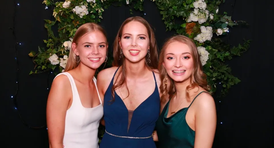 Tre studentesse della Middleton Grange School in abiti formali si trovano davanti a uno sfondo fiorito.