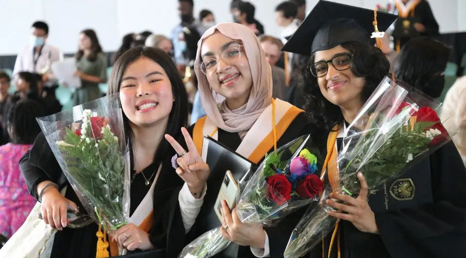 Un gruppo di diplomate in tocca e toga con fiori si trova nel campus del Fort Richmond Collegiate.