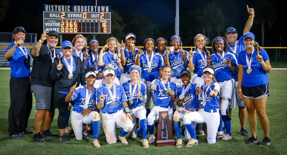 Studentesse della Trinity Christian Academy festeggiano la loro vittoria a softball davanti allo scenario di un centro storico.