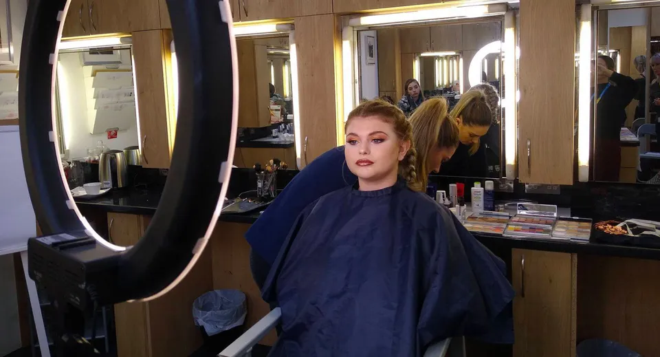 Una donna con i capelli biondi sta davanti a uno specchio nel salone dell'East Sussex College Eastbourne.