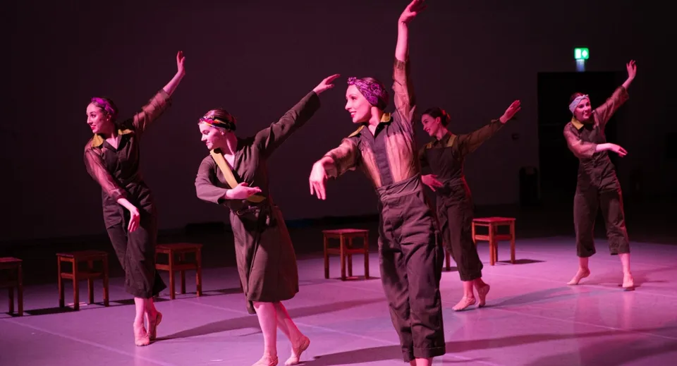 Un gruppo di ballerine del Seaford College esegue un movimento sincronizzato a braccia alzate su un palco.