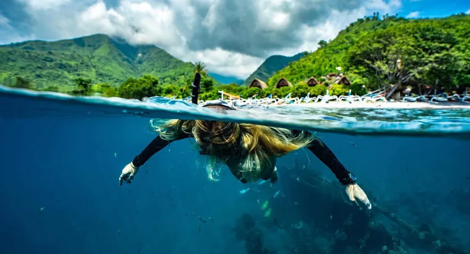 Una studentessa della Maleny State High School nuota in un'acqua limpida e blu davanti a montagne verdi e un cielo nuvoloso.