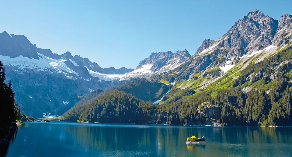 Un idrovolante giallo galleggia su un lago di montagna blu circondato da cime innevate vicino alla Abbotsford School of Integrated Arts.