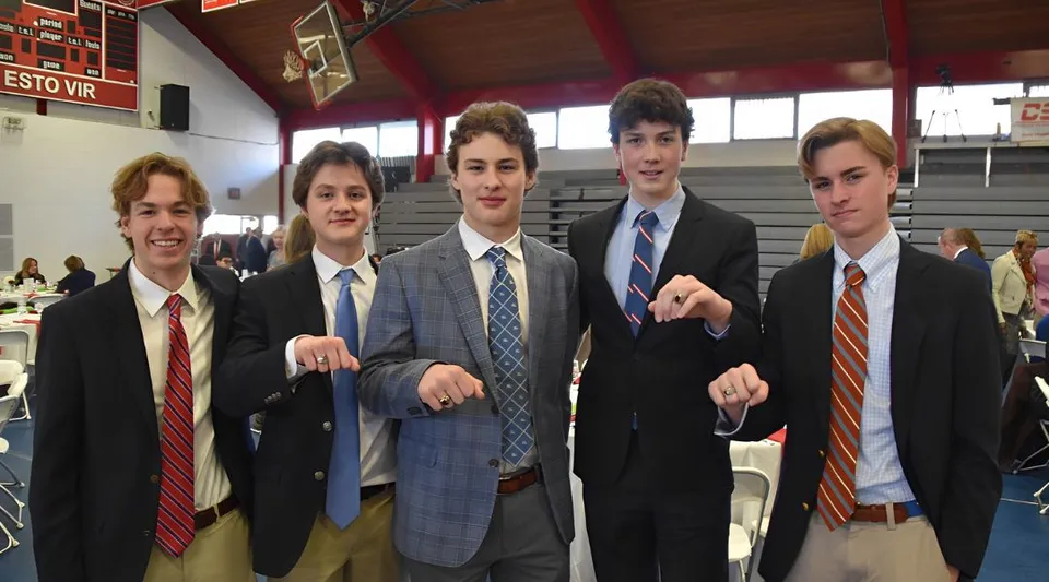 Un gruppo di studenti della Chaminade College Preparatory School si trova in abito formale in un ambiente scolastico con un canestro da basket sullo sfondo.