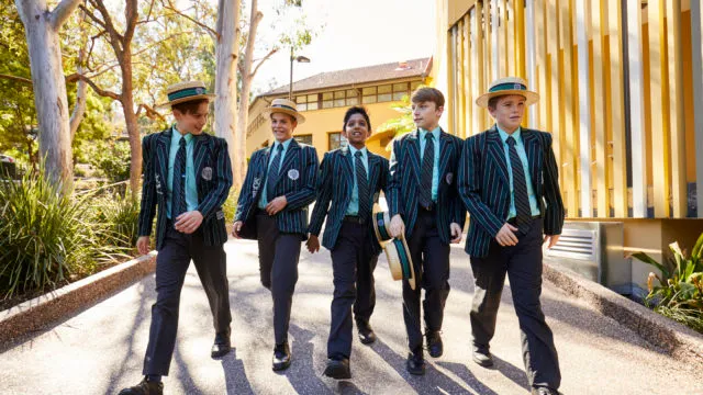 Un grupo de estudiantes del Brisbane Boys' College camina junto por un camino, rodeado de árboles y edificios.