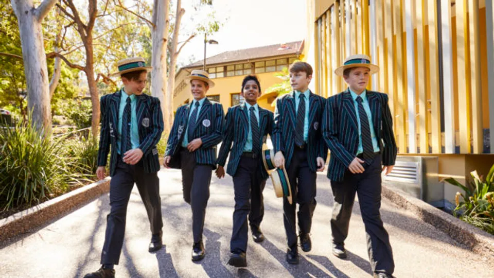Un gruppo di studenti del Brisbane Boys' College cammina lungo un viale, circondato da alberi ed edifici.