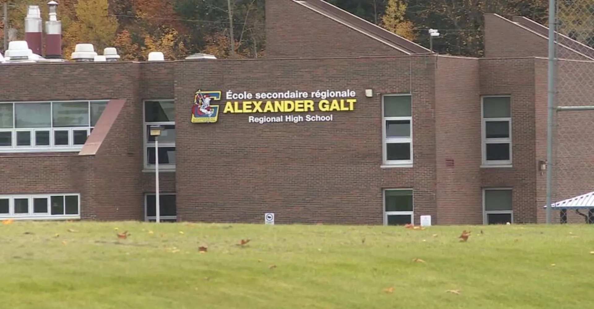 Il grande edificio in mattoni della Alexander Galt Regional High School è circondato da un prato con foglie autunnali.