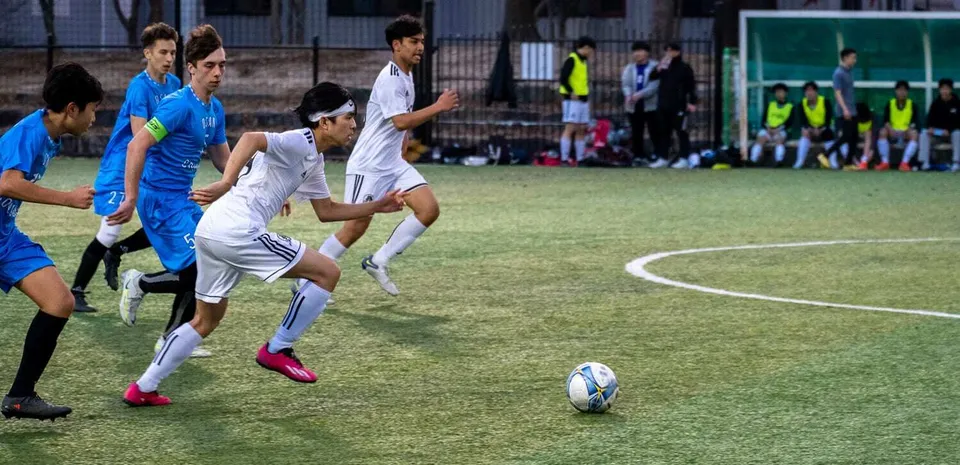 Schüler der Taejon Christian International School spielen ein Fußballspiel auf einem Rasenfeld mit Zuschauern im Hintergrund.