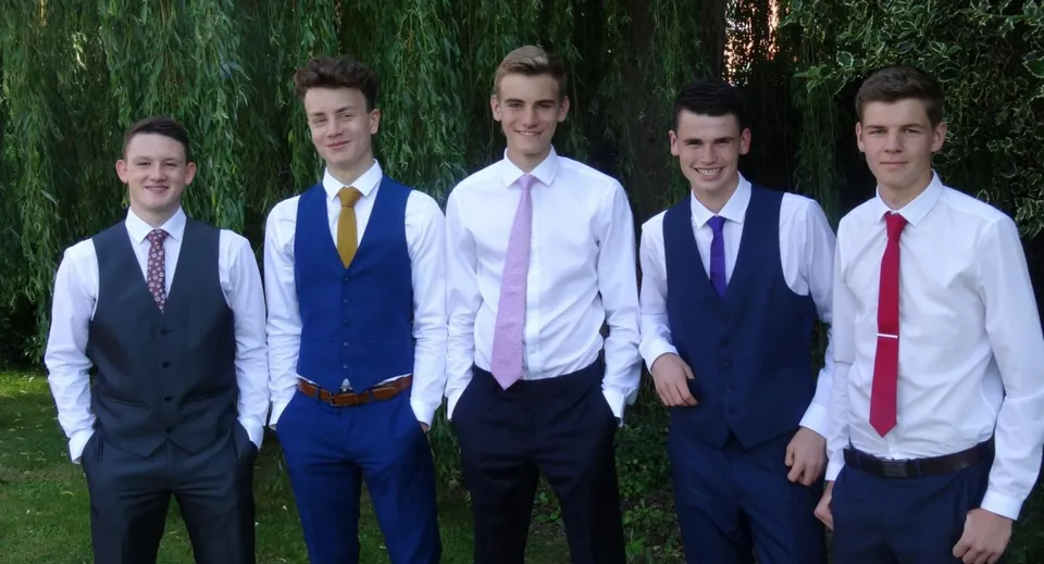 Un gruppo di cinque ragazzi in abiti formali si trova nel campus della Westlake Boys High School davanti ad alberi verdi.