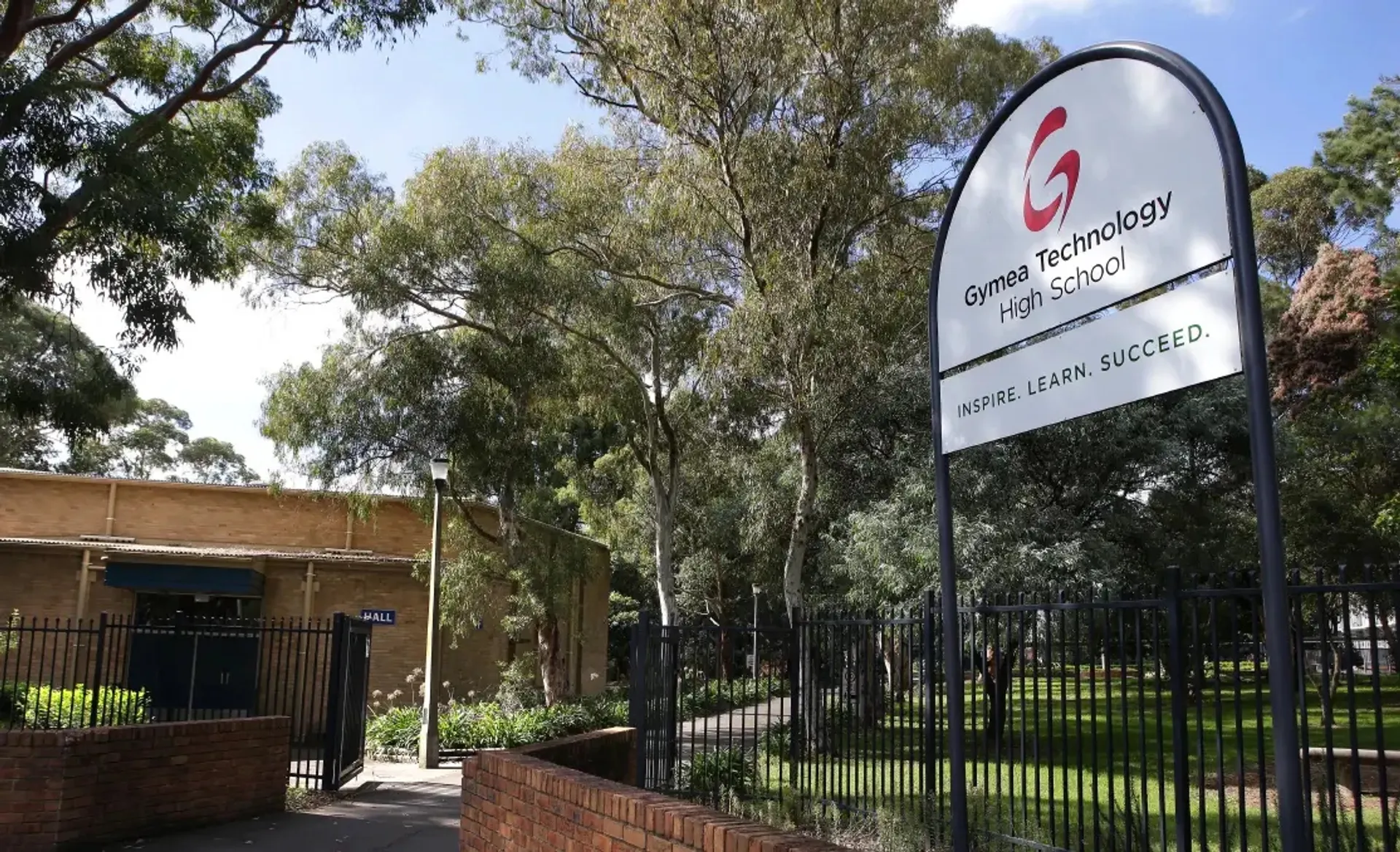 Il cartello d'ingresso della Gymea Technology High School accanto a una recinzione circondata da alberi.