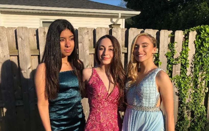Tres alumnas de Shore Regional High School posan frente a una cerca de madera con vegetación verde de fondo.