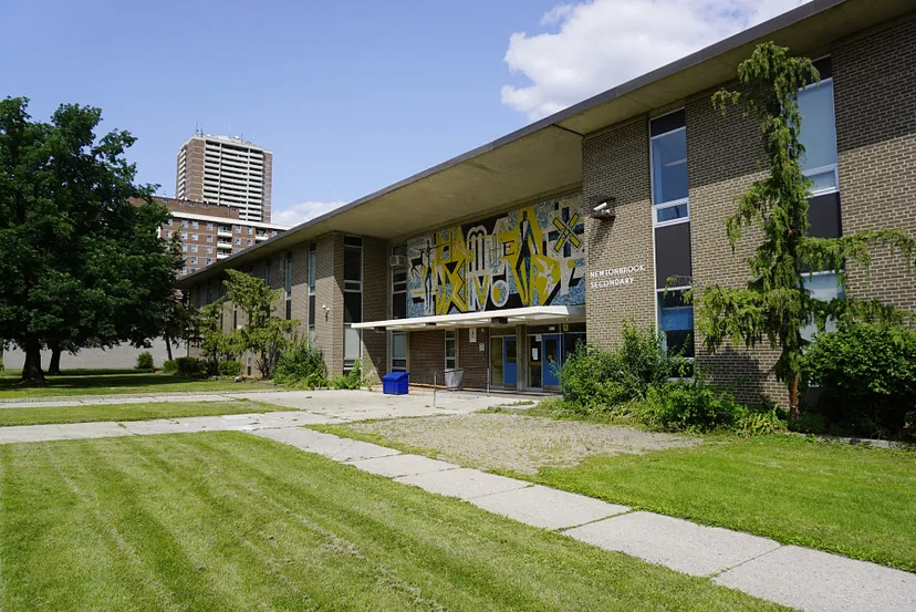 L'edificio in mattoni della Newtonbrook Secondary School con grandi finestre e murales colorati, circondato da un prato ben curato e alberi.
