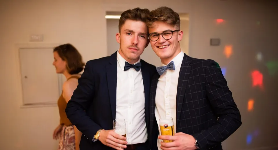 Due giovani uomini in abito formale partecipano a una festa nel campus della Merchiston Castle School con delle bevande in mano.