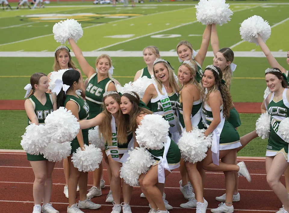 Un gruppo di cheerleader della Melbourne Central Catholic High School posa insieme sul campo sportivo con i pon-pon alzati.
