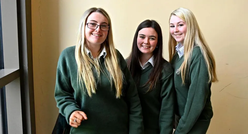Tre studentesse in divisa scolastica verde sorridono insieme nel corridoio della St. Mary's Holy Faith Killester.