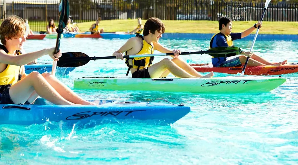 Studenti della Lynwood Senior High School durante attività acquatiche con kayak colorati in una piscina all'aperto.