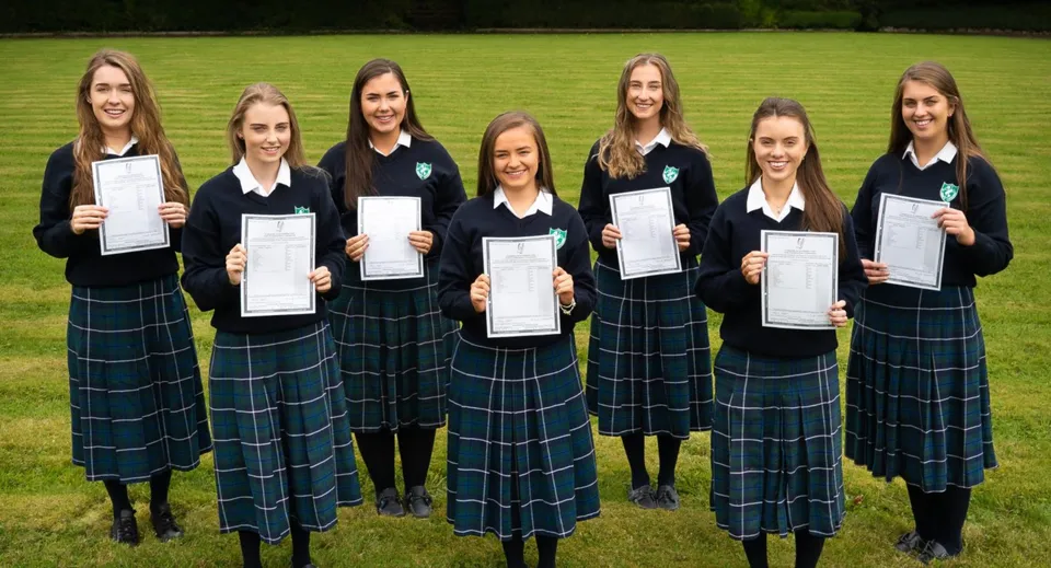 Sei studentesse della St. Anne's Secondary School sono all'aperto e mostrano i loro certificati immerse nel verde.