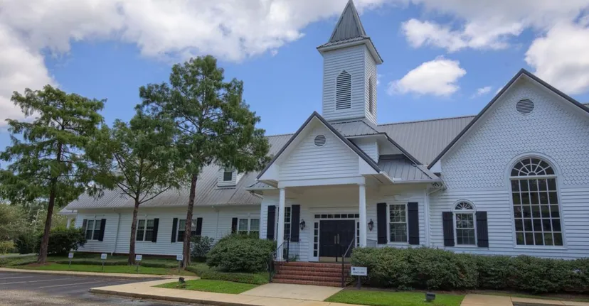 Una chiesa di legno bianca con un'alta torre sorge nel campus della Bayshore Christian School in un'area erbosa.