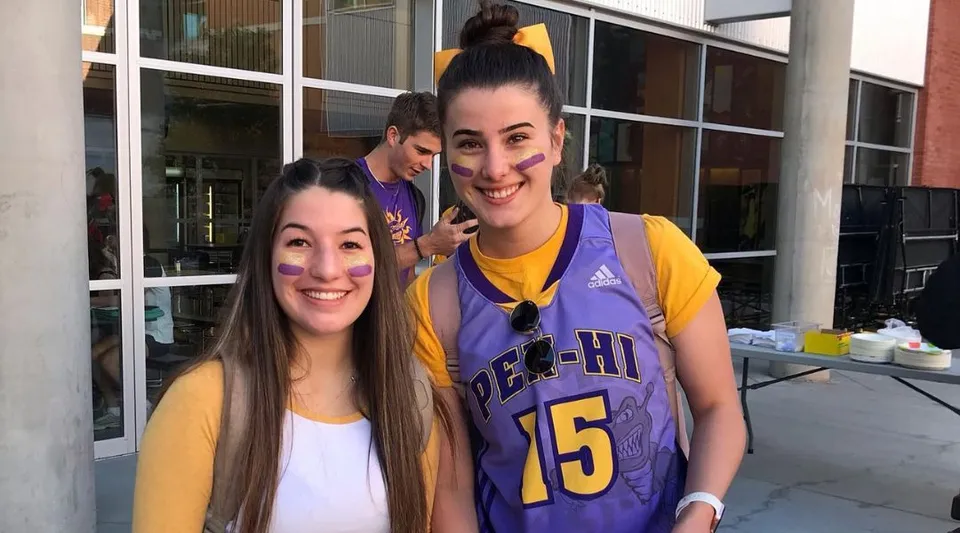 Due studentesse della Penticton Secondary School sorridono davanti a un edificio con grandi finestre.