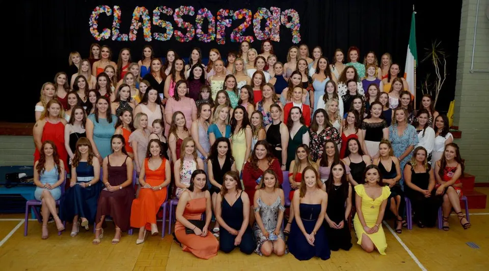 Un grande gruppo di studentesse della Sacred Heart School posa con abiti colorati in una palestra davanti alla scritta CLASSOF2020.