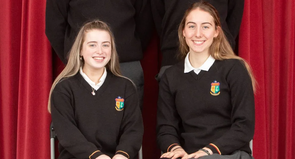 Due studentesse in divisa scolastica nera sono davanti a una tenda rossa nel campus della Our Lady’s Secondary School.