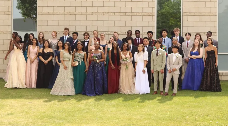 Un grande gruppo di studenti e studentesse della Huntsville School si trova in abiti formali su un prato davanti a un edificio in mattoni.
