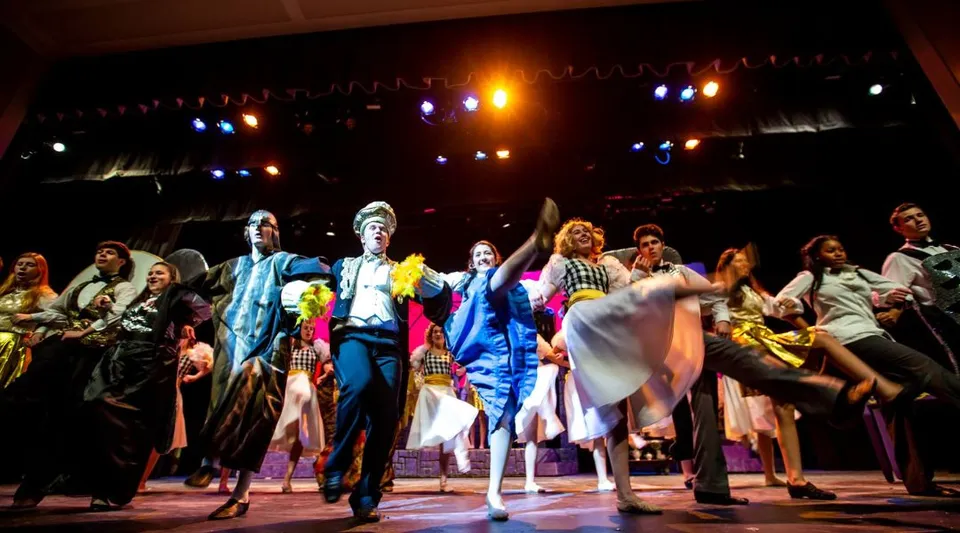 Un gruppo di studenti della North Shore Country Day School si trova in costumi colorati sul palco del teatro.