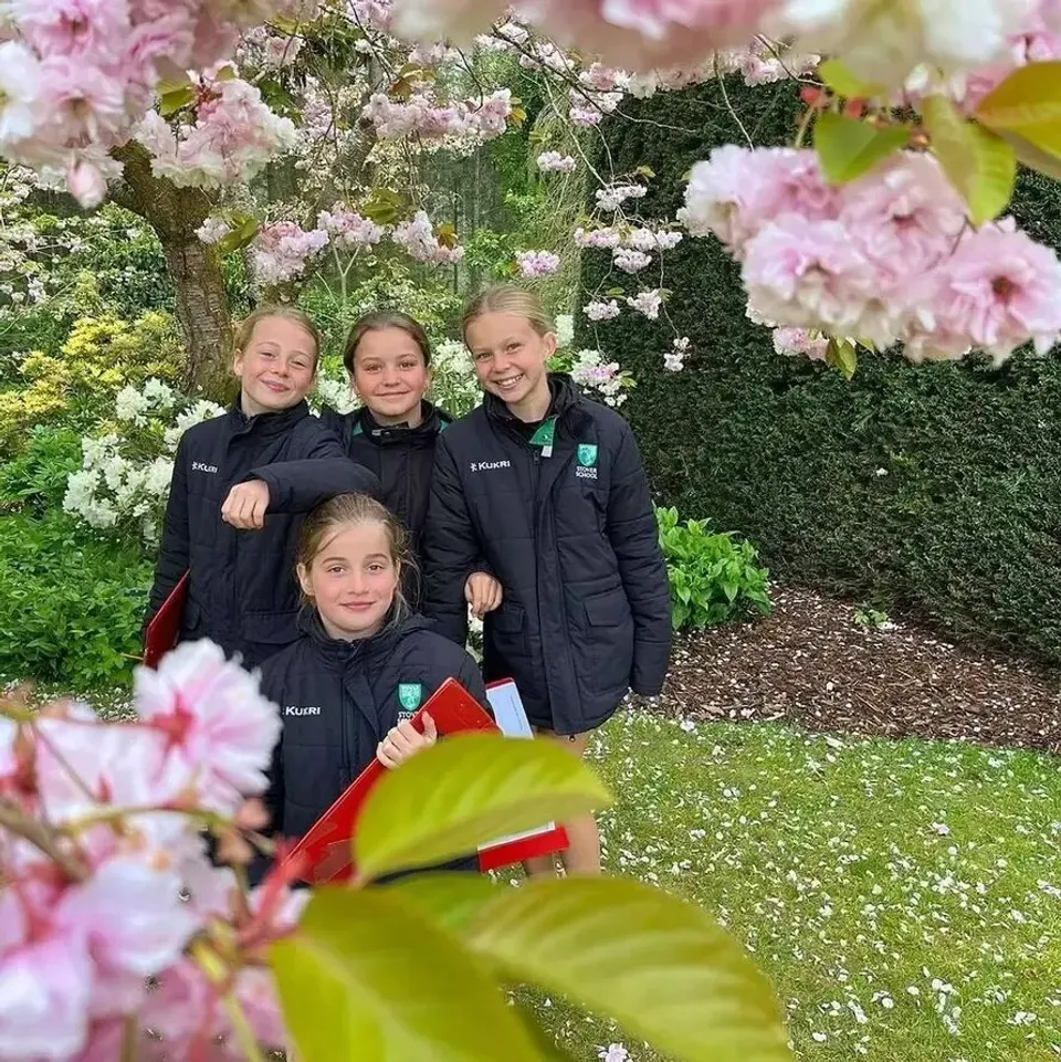 Quattro giovani studentesse della Stover School sono in piedi con giacche scolastiche scure sotto un ciliegio in fiore nel giardino del campus.