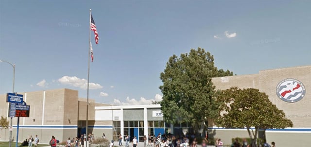Die amerikanische Flagge weht über dem mehrstöckigen Gebäude der El Camino Real Charter High School mit Bäumen und Menschen im Vordergrund.
