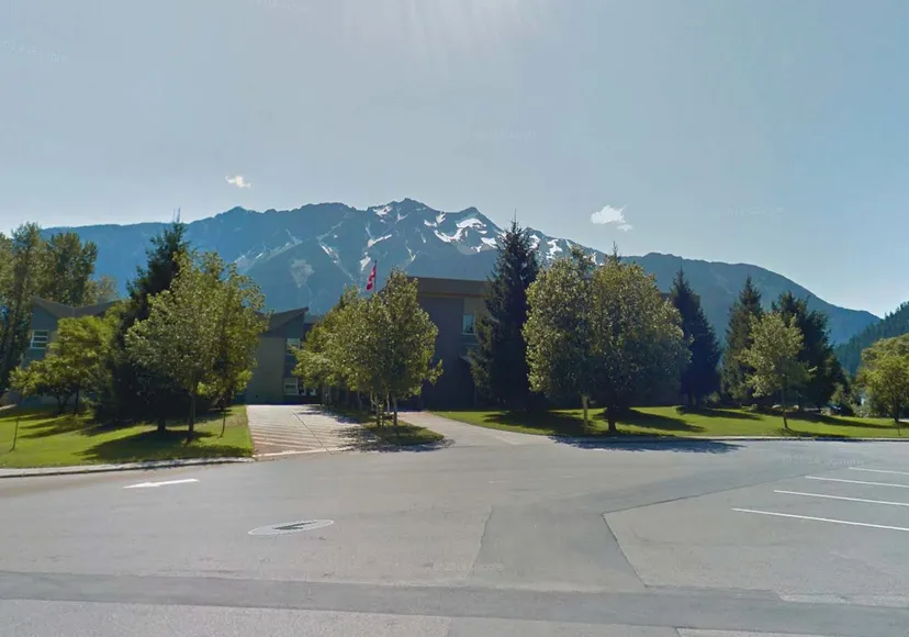 Un sentiero pavimentato conduce attraverso un paesaggio verde verso le montagne nel campus della Pemberton Secondary School.