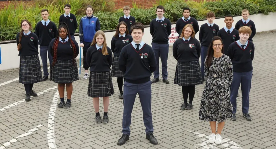 Un gruppo di studenti e studentesse del Presentation College Carlow insieme in un'area esterna pavimentata con zone verdi.