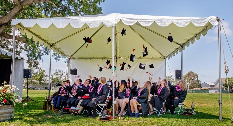 Studenti della Dunn School seduti all'aperto sotto un grande tendone bianco durante la cerimonia di diploma.