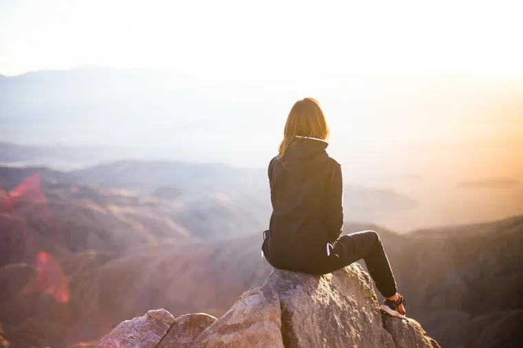 Frau sitzt auf einem Felsen und blickt über Berge im Sonnenlicht