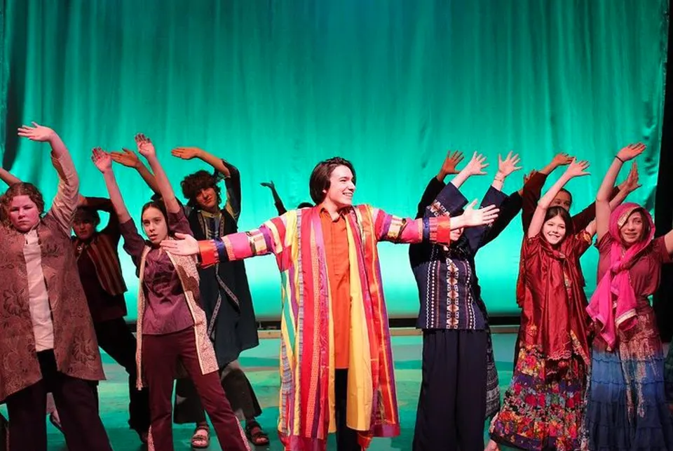 Un gruppo di studenti della Okanagan Mission Secondary School si esibisce su un palco con sfondo verde.