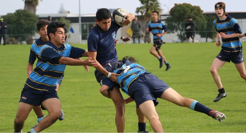 Gli studenti del Sancta Maria College giocano una partita di rugby sul campo sportivo davanti agli edifici scolastici.