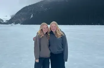 Dos chicas abrazadas sobre un lago helado con una ladera boscosa al fondo