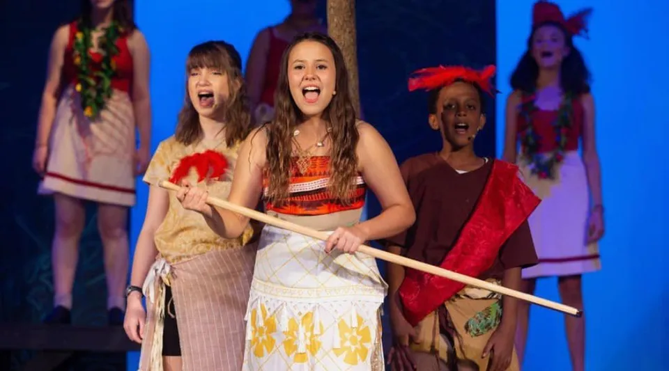 Un gruppo di studentesse della Providence Christian Academy si esibisce sul palco con costumi colorati davanti a uno sfondo blu.