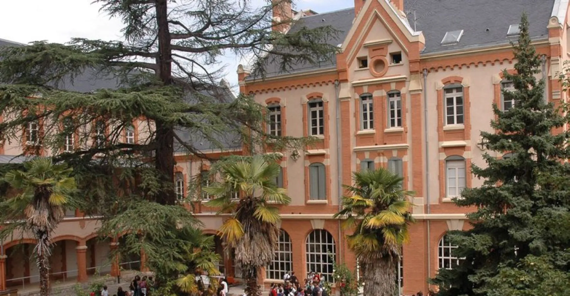 L'edificio del Lycée Gabriel Fauré è una grande struttura rosa con finestre ad arco, circondata da palme e verde vegetazione.
