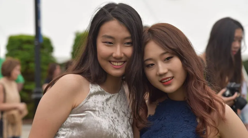 Due studentesse con lunghi capelli scuri sorridono insieme davanti alle aree verdi del campus della St. Mark's School.
