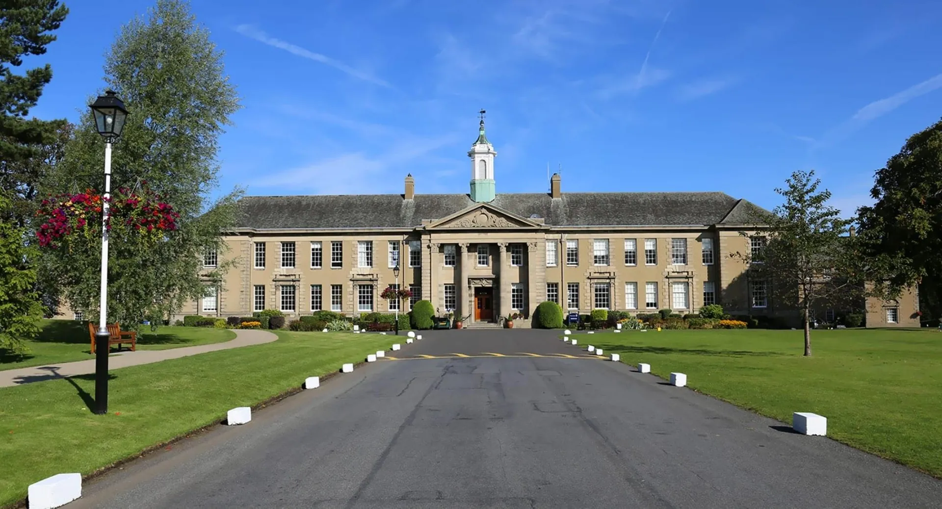 L'edificio principale storico della Merchiston Castle School con la sua torre centrale sorge su un prato curato circondato da alberi.