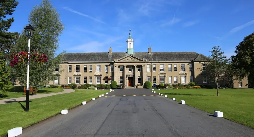 L'edificio principale storico della Merchiston Castle School con la sua torre centrale sorge su un prato curato circondato da alberi.